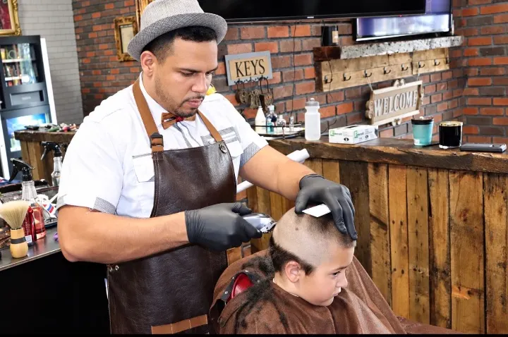 Barber giving a young boy a haircut with clippers at NY Styles Barbershop in Medford, NY